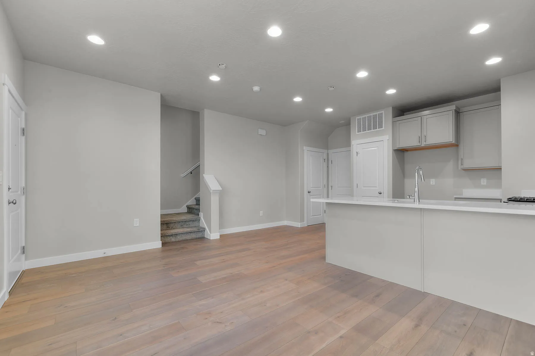 Open-concept living area featuring wood-finish flooring, recessed lighting, a modern kitchen island with an undermount sink, light-toned cabinetry, and a staircase with carpeted treads