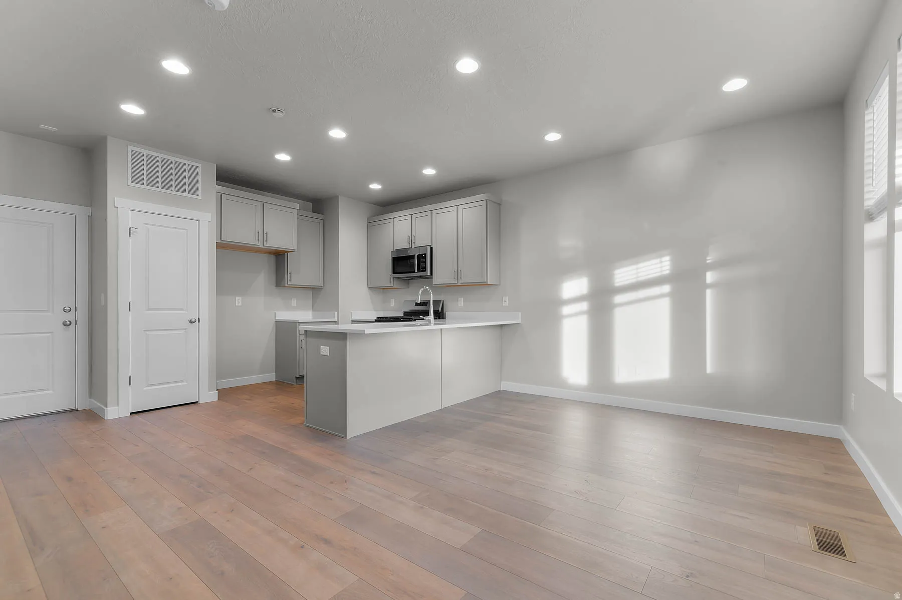 Open-concept living space featuring wood-finish flooring, recessed lighting, and multiple windows with blinds