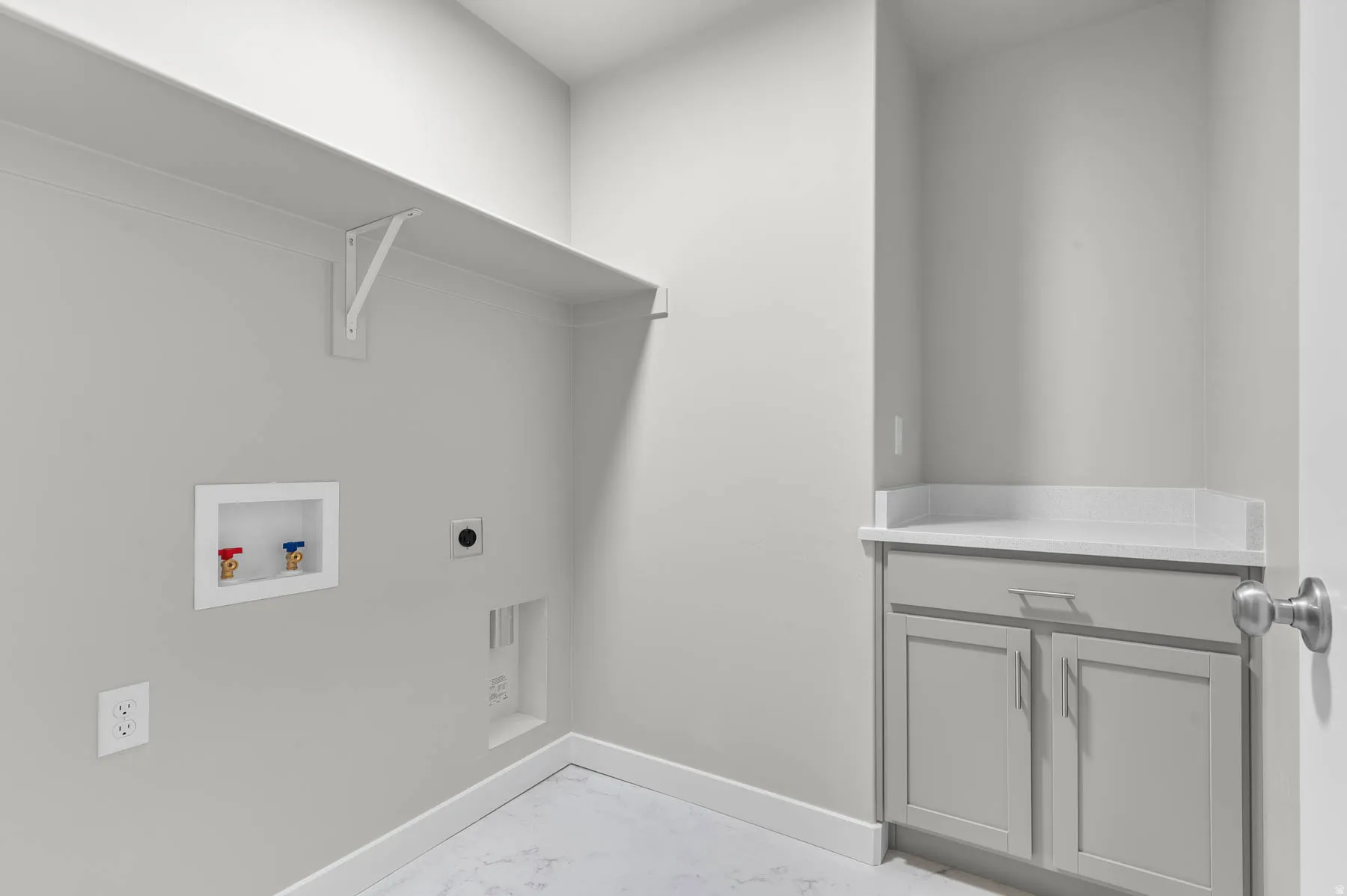 Dedicated laundry area featuring a built-in shelf, light gray cabinetry, a white countertop, and a utility sink rough-in