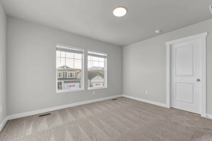 Light gray interior walls with white trim, two clear glass windows, neutral patterned carpet, white two-panel interior door, and a flush-mount ceiling light fixture
