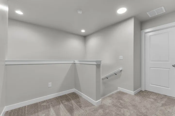 Carpeted landing area featuring a white paneled door, flush-mounted ceiling lights, a white handrail, and baseboard trim