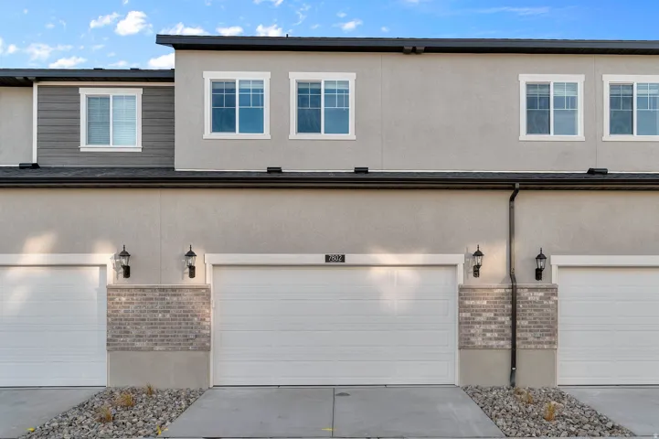 Contemporary townhome exterior featuring light gray stucco, multiple white-framed windows, and a black shingled roof