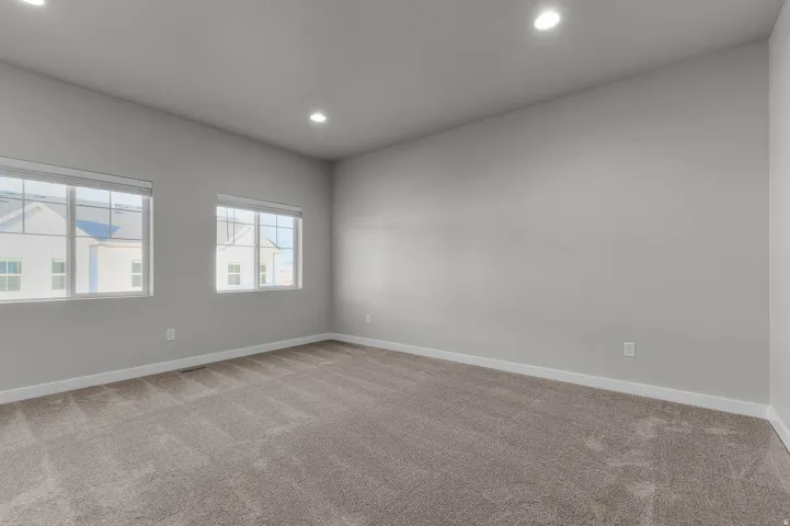 Spacious room featuring neutral carpeting, light gray walls, and two large windows with white blinds