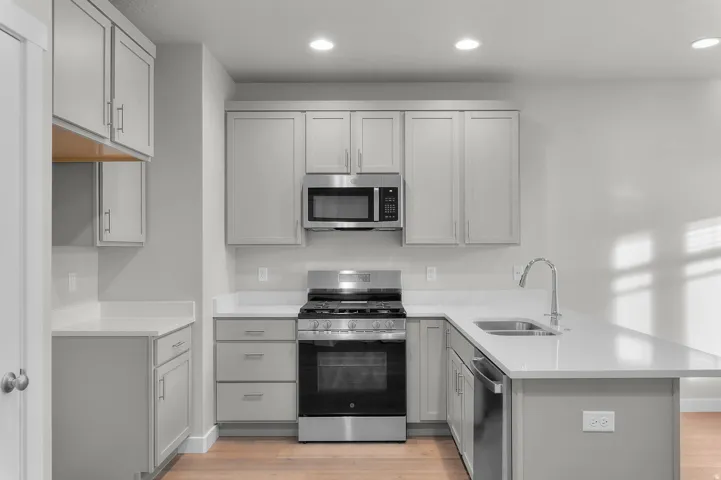Modern kitchen featuring light gray cabinetry, stainless steel appliances, white countertops, and wood-finish flooring