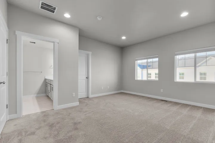 Spacious carpeted room featuring two windows, recessed lighting, and a doorway revealing a vanity with an undermount sink