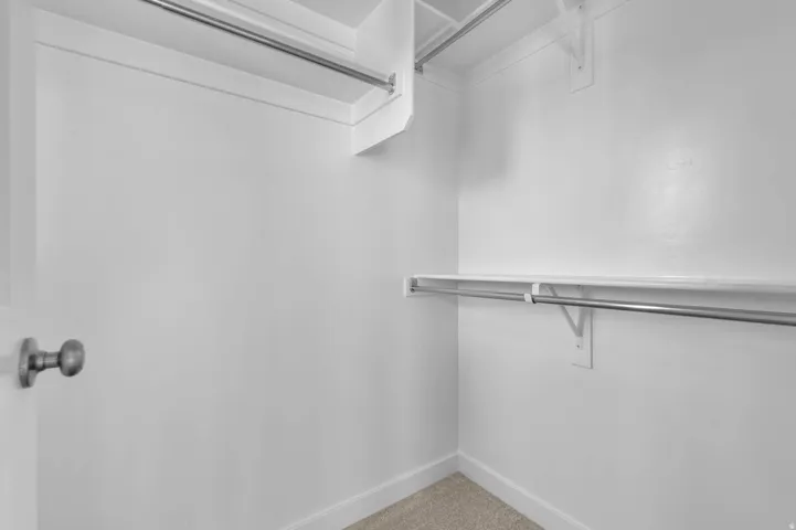 Walk-in closet featuring white painted walls, a light-toned carpet, and a white baseboard trim