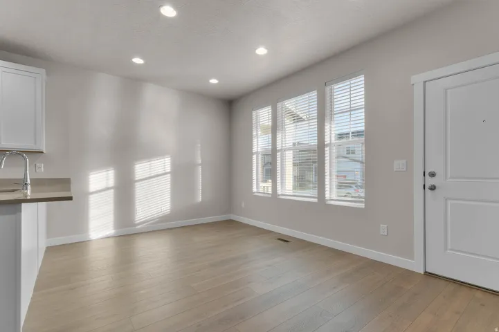 Open-concept living space with light wood-finish flooring, recessed lighting, and three large windows with blinds