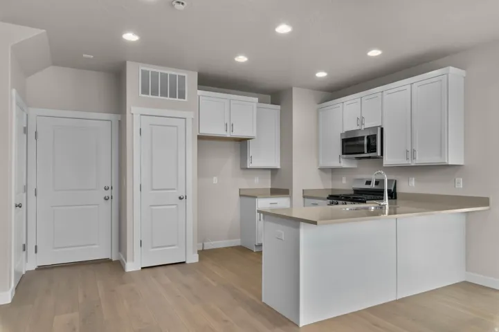 Contemporary kitchen featuring light wood-finish flooring, white cabinetry, a built-in stainless steel microwave, and an island with an integrated sink and breakfast bar