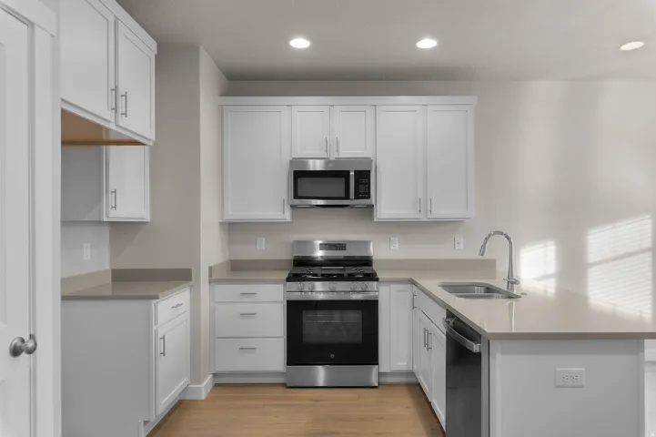Modern kitchen featuring white shaker cabinetry, stainless steel appliances, light-toned countertops with a matching backsplash, and wood-finish flooring