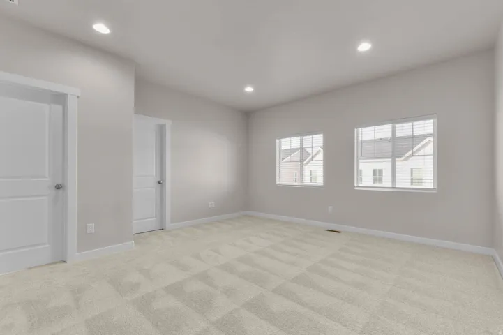 Spacious room featuring neutral carpeting, two paneled doors with white trim, recessed lighting, and two windows with blinds