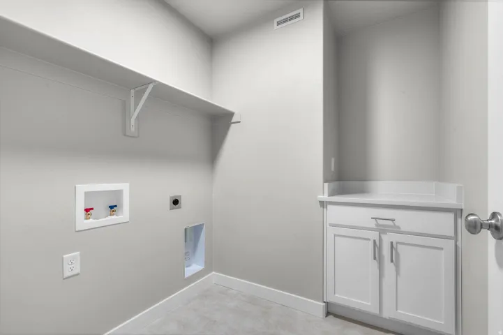 Dedicated laundry area featuring a wall-mounted shelf, utility sink hookups, and a white base cabinet with a light-toned countertop