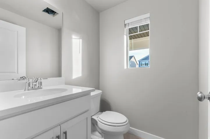 Bathroom vanity featuring a white countertop with an integrated sink, chrome faucet, white paneled cabinetry, and a rectangular mirror