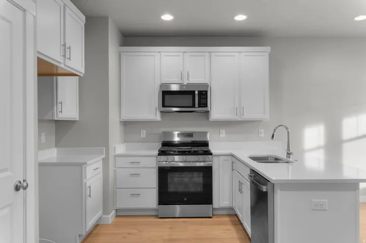 Contemporary kitchen featuring white cabinetry with brushed nickel hardware, light-toned countertops, stainless steel appliances, and wood-finish flooring