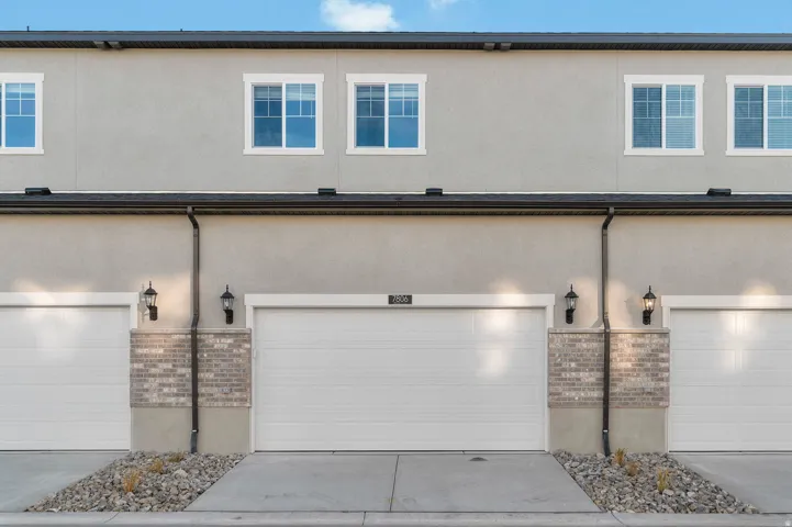 Stucco exterior featuring multiple windows with white trim, a black roofline, and attached garages