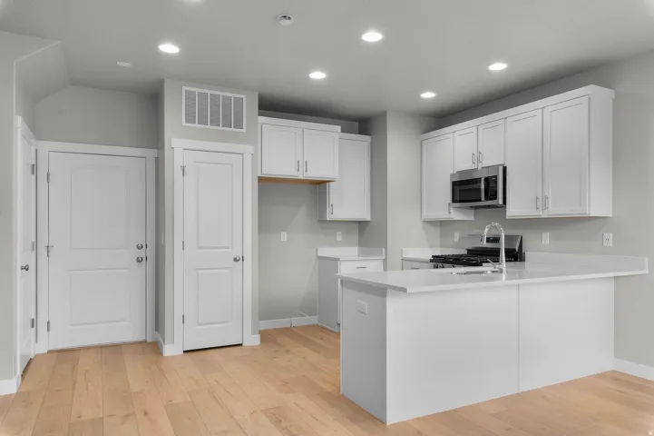 Contemporary kitchen featuring white cabinetry, stainless steel microwave, gas range, and a central island with a sink