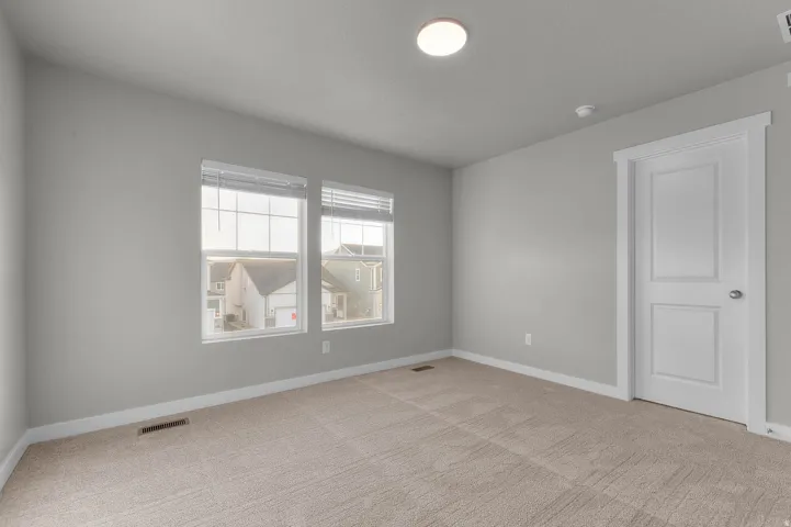Carpeted room featuring two windows with blinds, a single panel door with decorative trim, and light gray painted walls