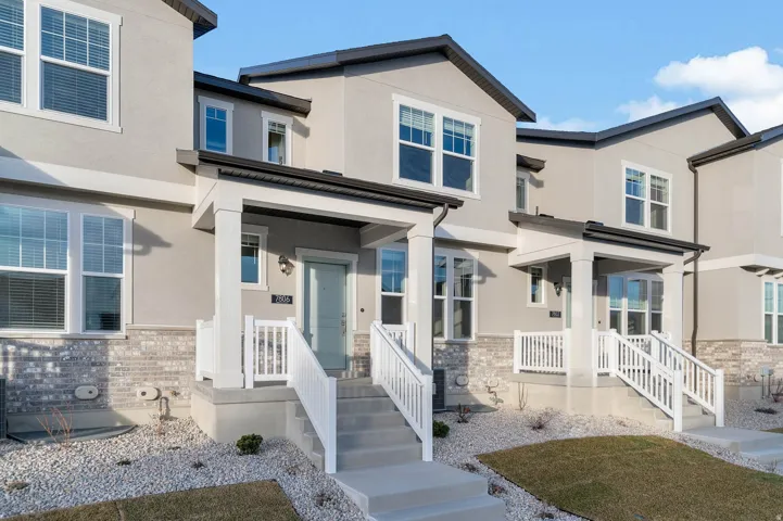 Modern townhome exterior with light gray siding, white trim, and a partial brick facade