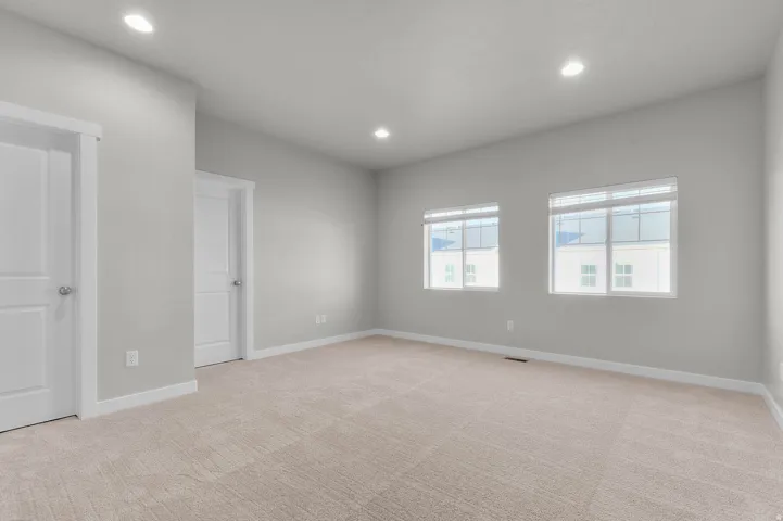 Spacious room featuring neutral carpeting, two panel doors with satin nickel hardware, recessed lighting, and two windows with white blinds