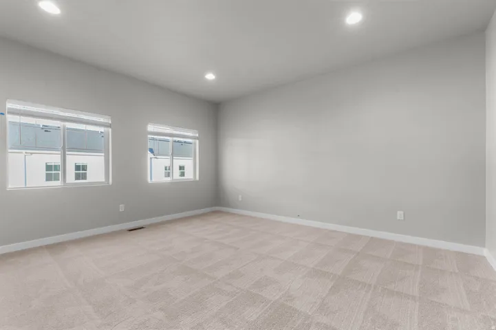 Spacious room featuring neutral carpeting, light gray walls, two windows with blinds, recessed lighting, and white baseboards