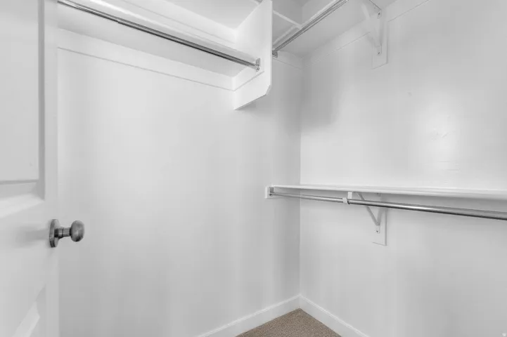 Walk-in closet featuring white painted walls, white shelving, and chrome hanging rods