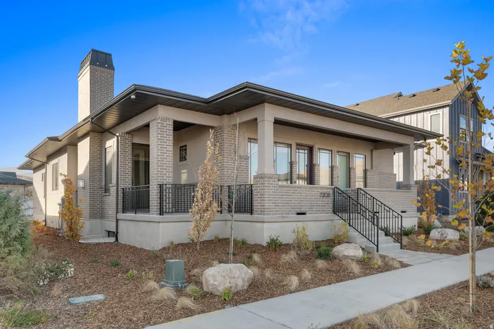 Contemporary residential exterior featuring a covered porch with brick columns and black metal railings