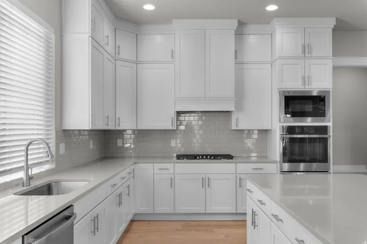Contemporary kitchen featuring white cabinetry, light-toned countertops, a stainless steel sink, a built-in oven, and a gas cooktop