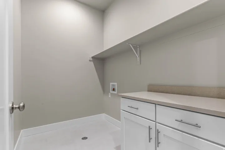 Utility room featuring a built-in countertop, white cabinetry with brushed nickel hardware, and an overhead shelf