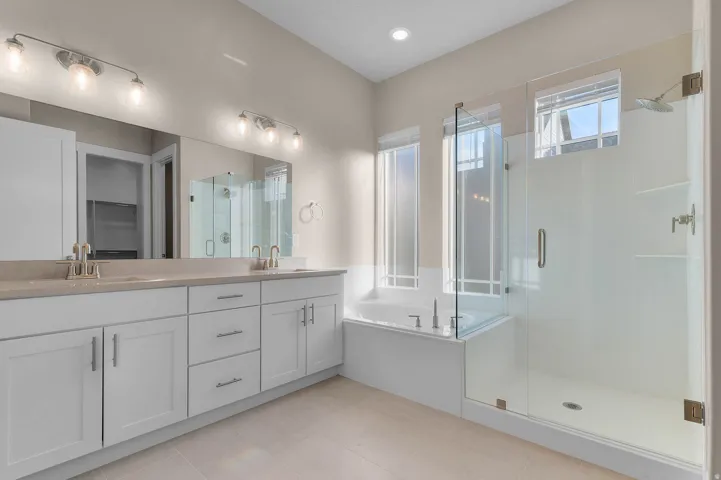 Bathroom featuring a dual vanity with light-colored countertops, a built-in soaking tub, and a glass-enclosed shower with a rainfall showerhead