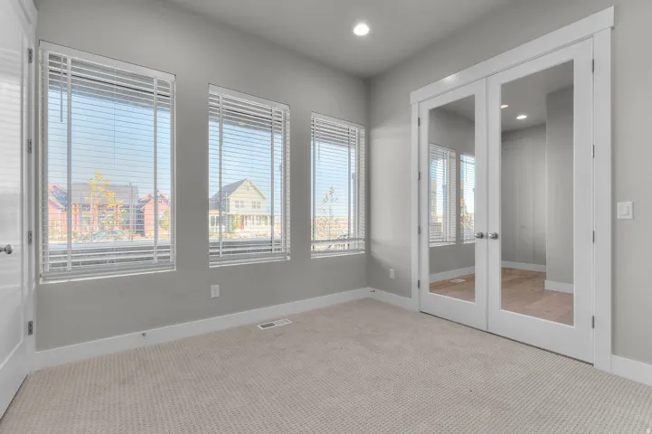 Light-toned carpeted room featuring three windows with blinds and white trim