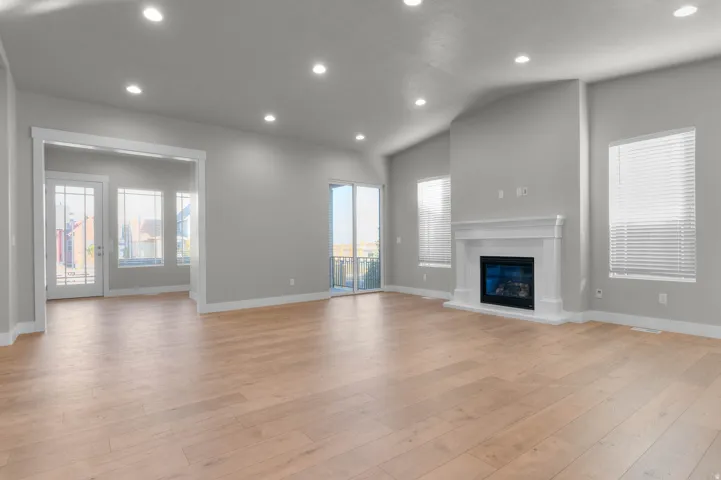 Spacious living area featuring light wood-finish flooring, a contemporary fireplace with a classic white mantel, and recessed lighting