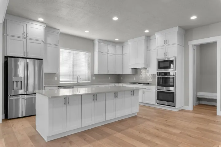 Kitchen featuring a central island, white shaker cabinetry, stainless steel appliances, and wood-finish flooring