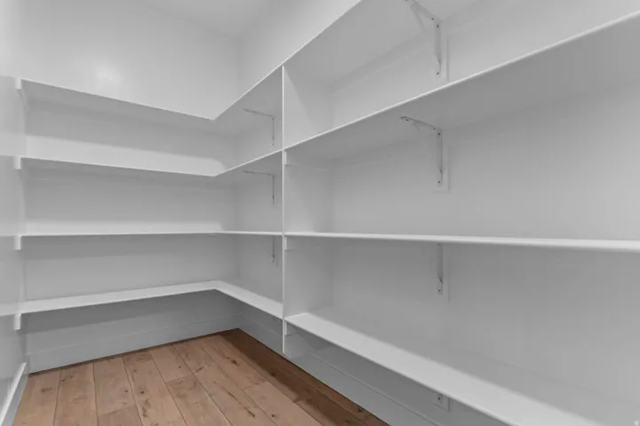 Walk-in pantry featuring extensive white shelving, corner storage, and wood-finish flooring