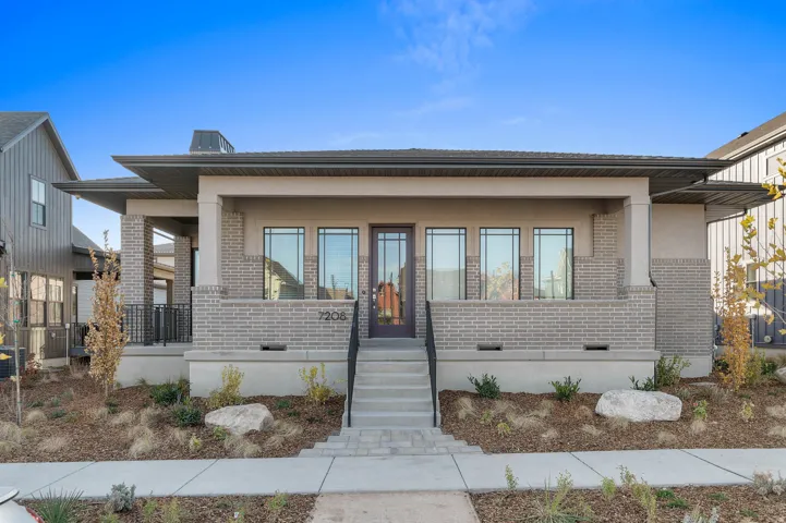 Contemporary exterior featuring a covered front porch, light gray brick accents, dark framed windows, and a prominent front door with vertical window panels