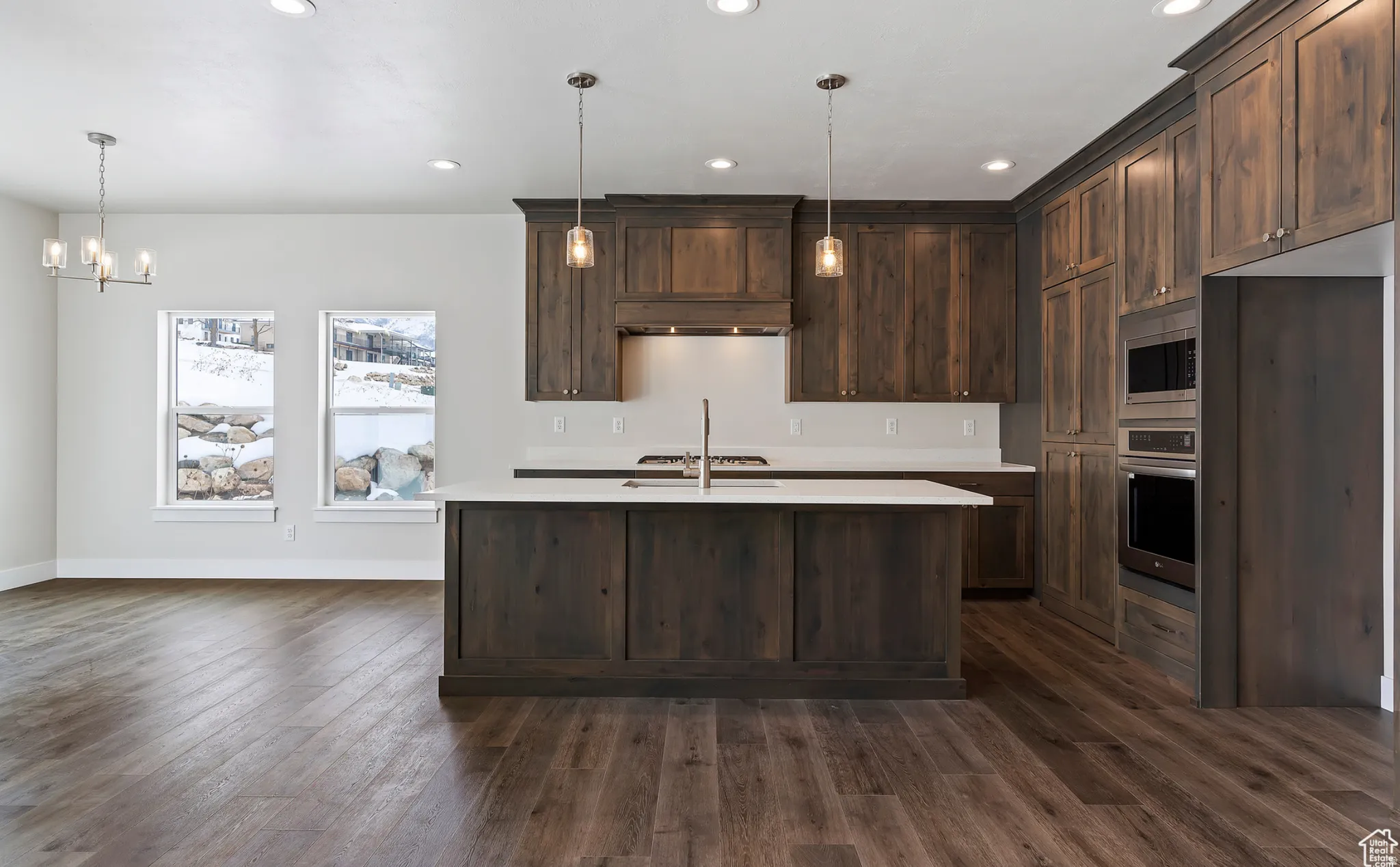 Kitchen with dark wood finish cabinetry, stainless steel appliances, a chandelier, and an island with sink