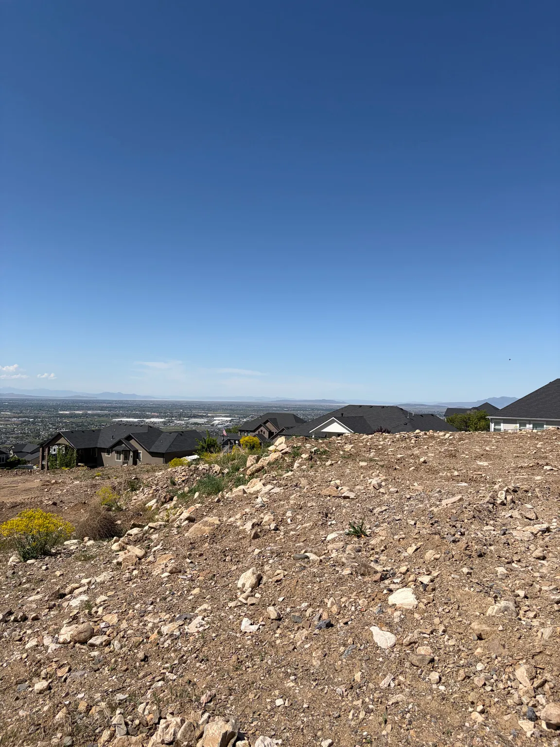 Elevated building lot featuring a clear blue sky, distant mountainous terrain, and surrounding residential structures