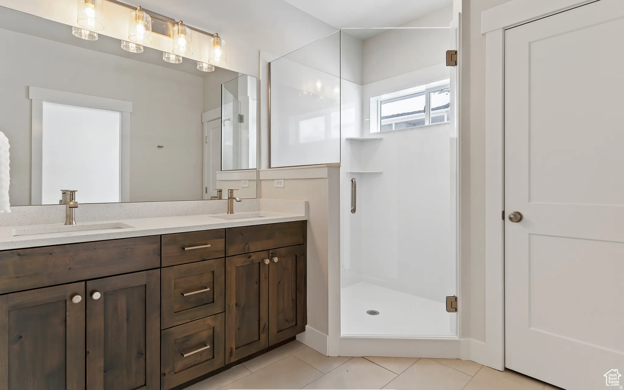 Full bathroom featuring double vanity, a stall shower, and light tile patterned floors