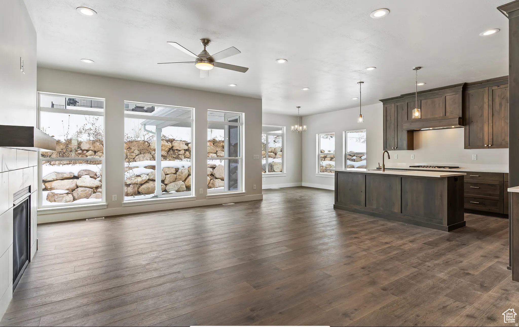 Unfurnished living room with ceiling fan, hanging lights, dark wood-type flooring, and a fireplace