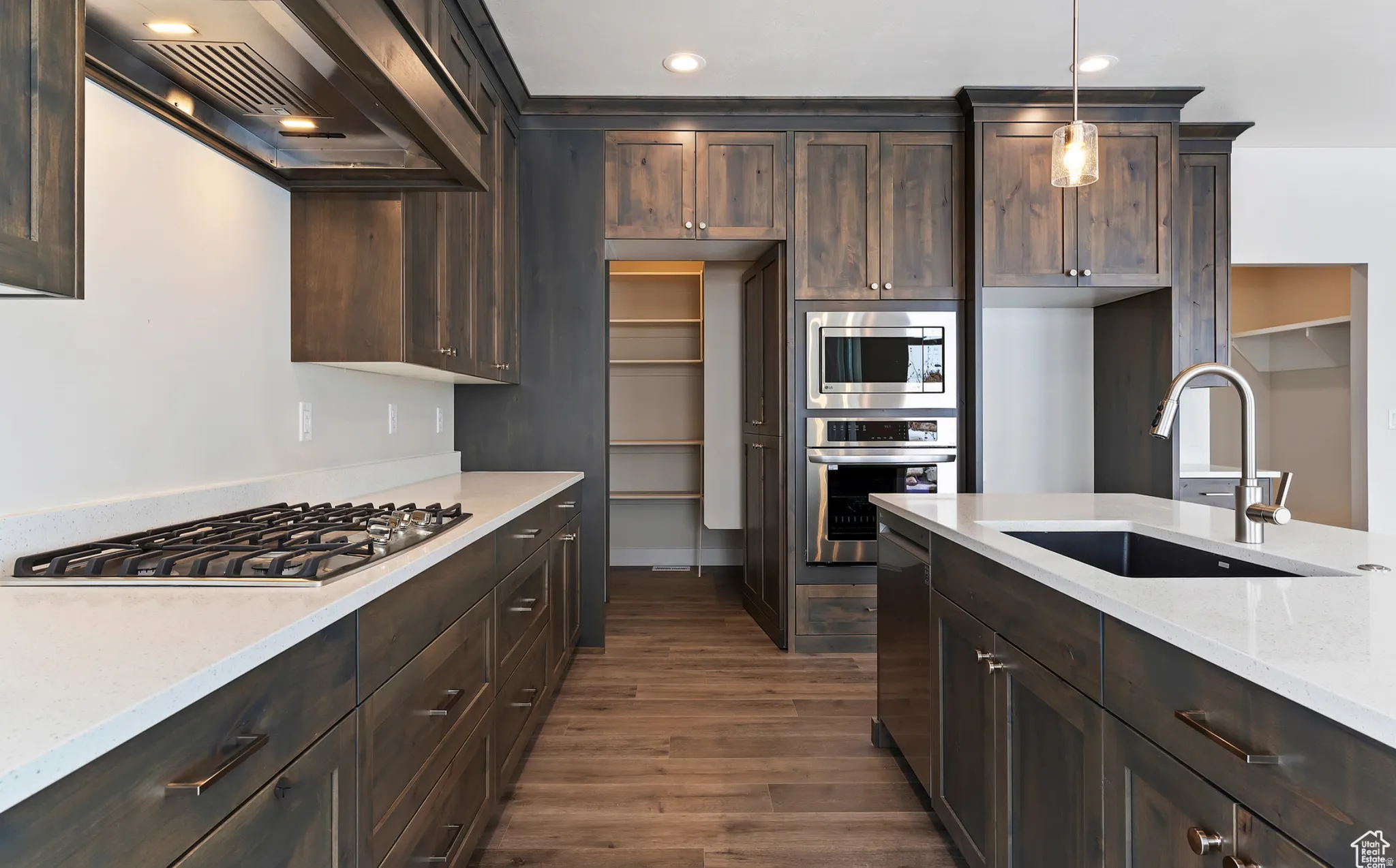 Kitchen featuring dark wood finish cabinetry, stainless steel appliances, light stone countertops, dark wood finished floors, and hanging light fixtures