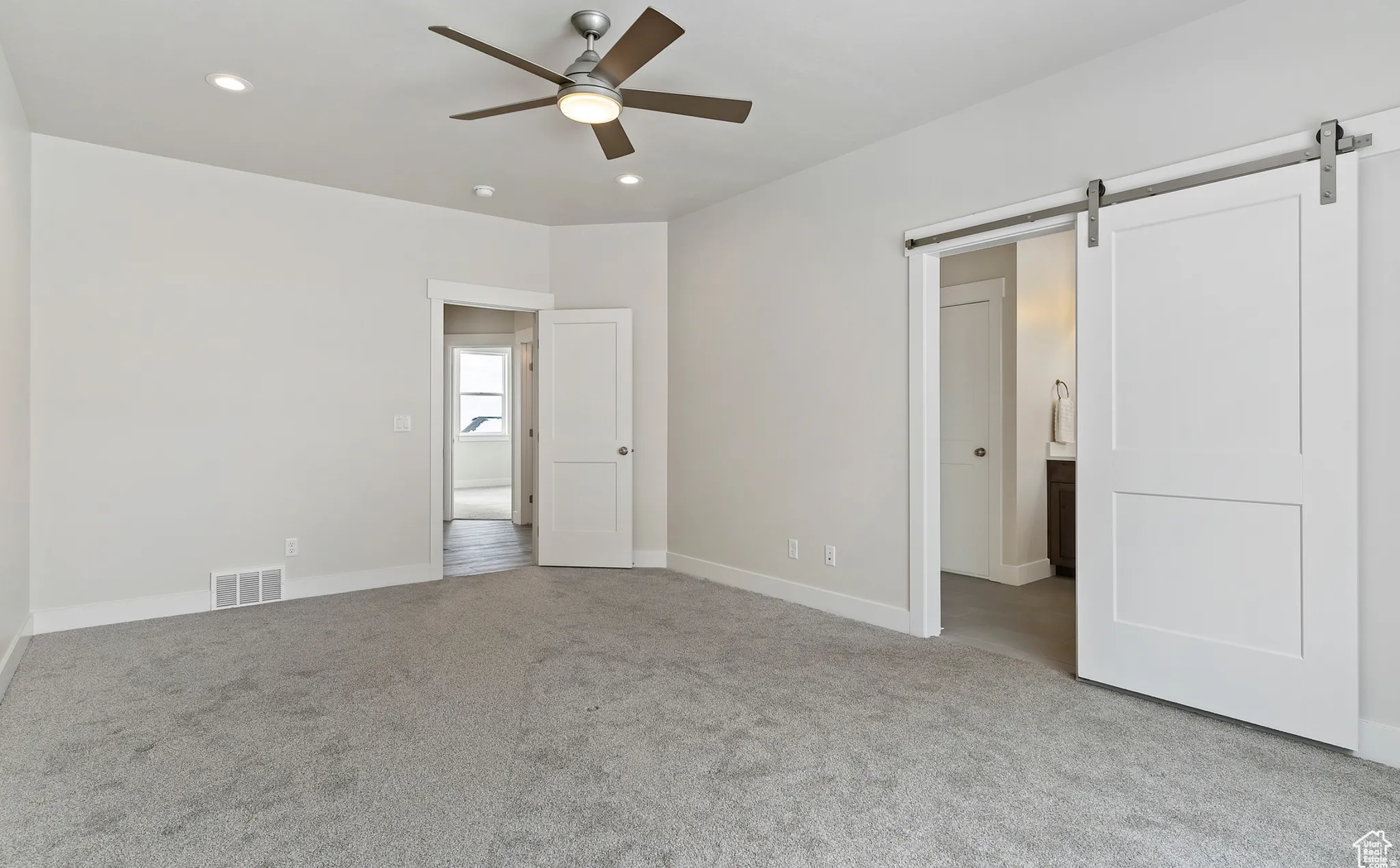 Unfurnished bedroom with a barn door, light colored carpet, recessed lighting, connected bathroom, and ceiling fan