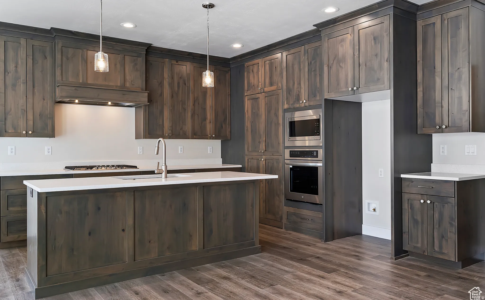 Kitchen with dark wood finish cabinetry, stainless steel appliances, a center island with sink, and hanging light fixtures