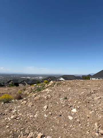 Elevated building lot featuring a clear blue sky, distant mountainous terrain, and surrounding residential structures