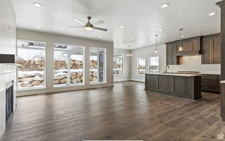 Unfurnished living room with ceiling fan, hanging lights, dark wood-type flooring, and a fireplace