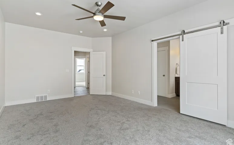 Unfurnished bedroom with a barn door, light colored carpet, recessed lighting, connected bathroom, and ceiling fan