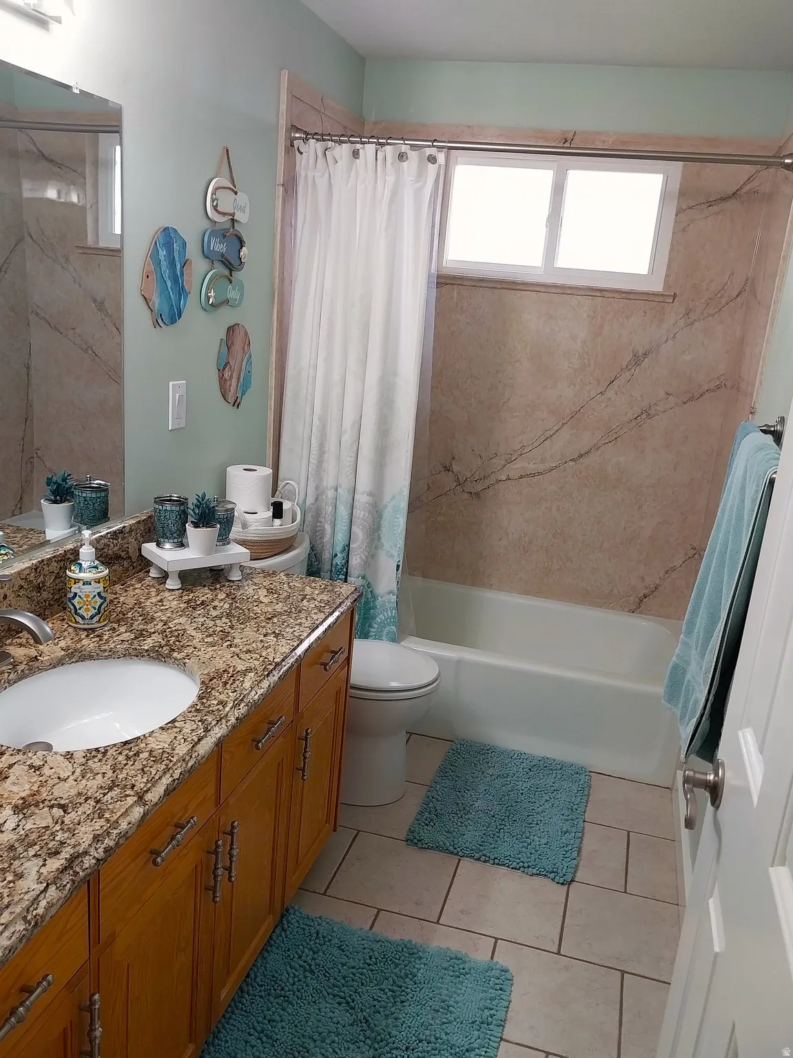 Bathroom with vanity, healthy amount of natural light, shower / tub combo with a marble finish souraund, and light tile patterned floors