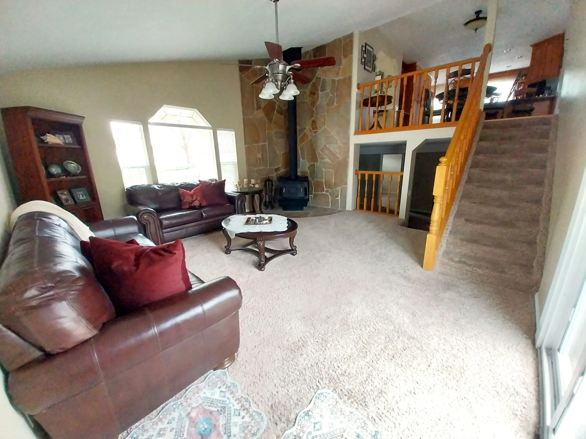 Living room with ceiling fan, a wood stove, lofted ceiling, and carpet