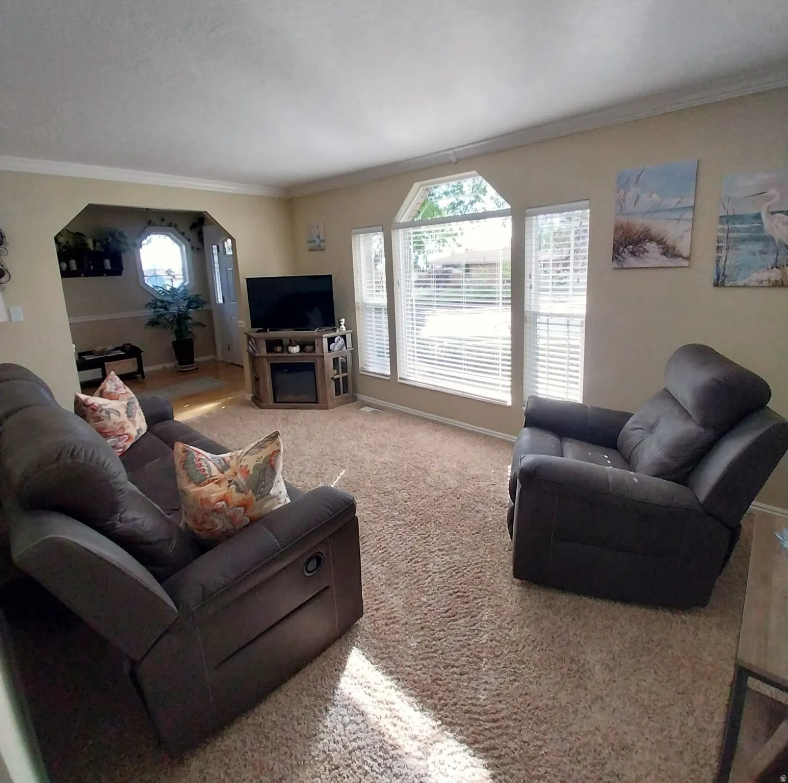 Living room with arched walkways, crown molding, and light colored carpet