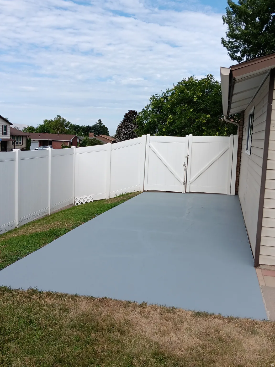 Paved outdoor RV parking with a light gray sealer/paint, enclosed by a white privacy fence with double gates