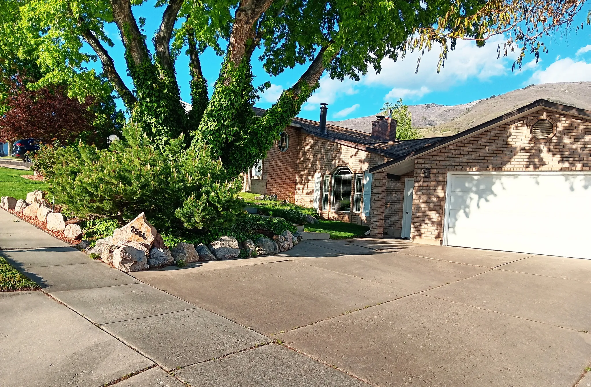 View of side of home featuring brick siding, a chimney, concrete driveway, lower entrance and a garage