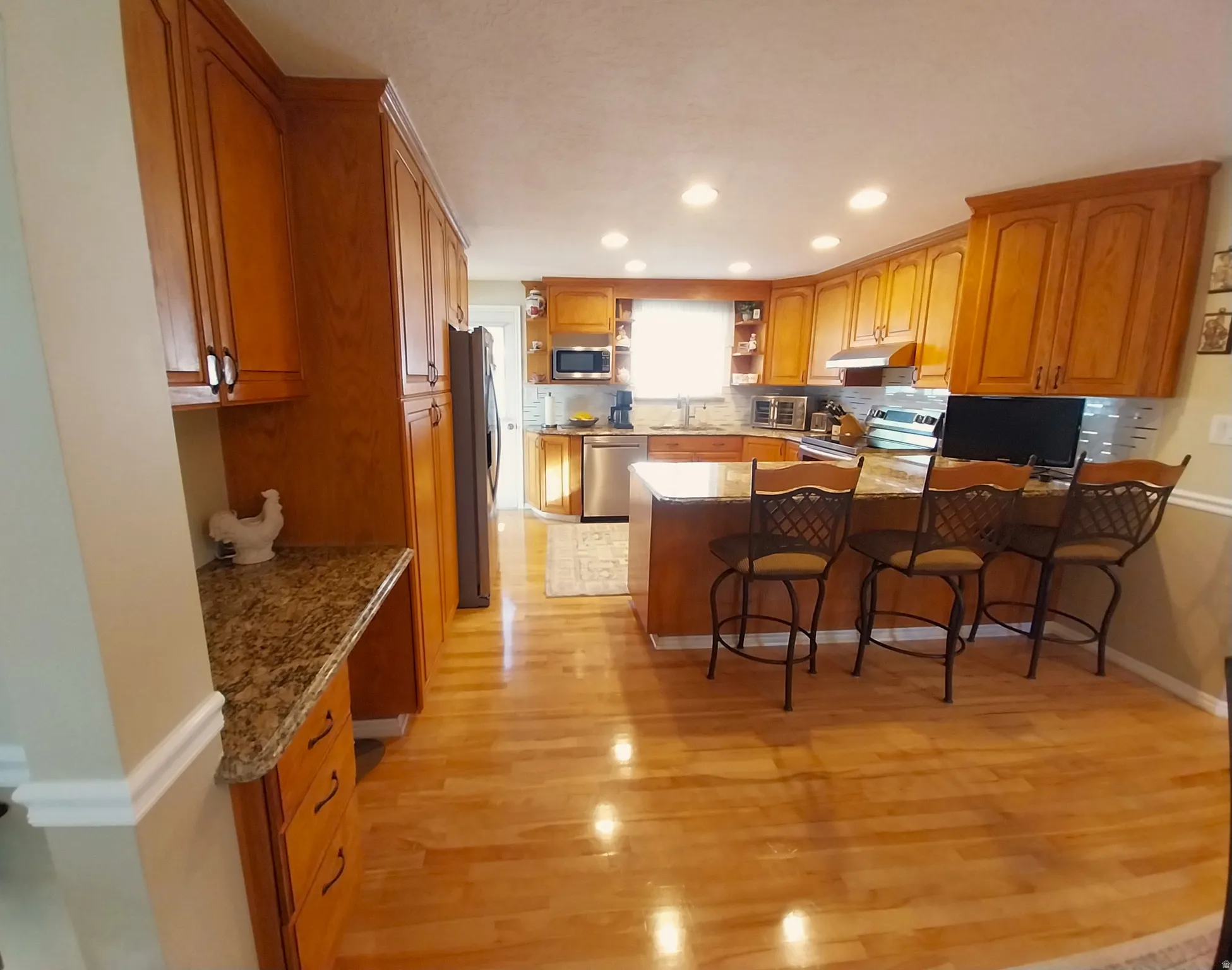 Kitchen featuring a peninsula, wood finish cabinets, open shelves, stainless steel appliances, and light wood finished floors