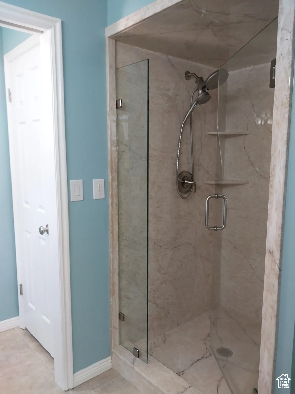 Glass-enclosed shower with stone-finish walls, built-in shelving, and a handheld showerhead